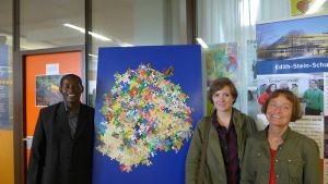 Foto: Father Jordan, Martina Meschenmoser, Irmgard Steinberger vor der UNESCO-Puzzle-Wand