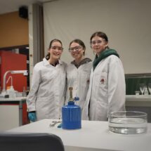 Drei lachende Schülerinnen in Laborkitteln posieren im Labor.