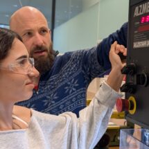 Ein Techniker weist eine Schülerin mit Schutzbrille an der Drehmaschine ein.