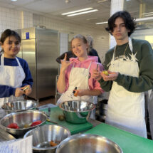 Kochprojekt: Eine Schülergruppe in weißen Schürzen schnippelt Gemüse.