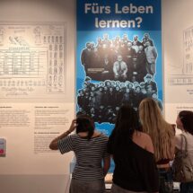 Innenansicht des Schulmuseums mit Schülerinnen, die Infotafeln studieren.